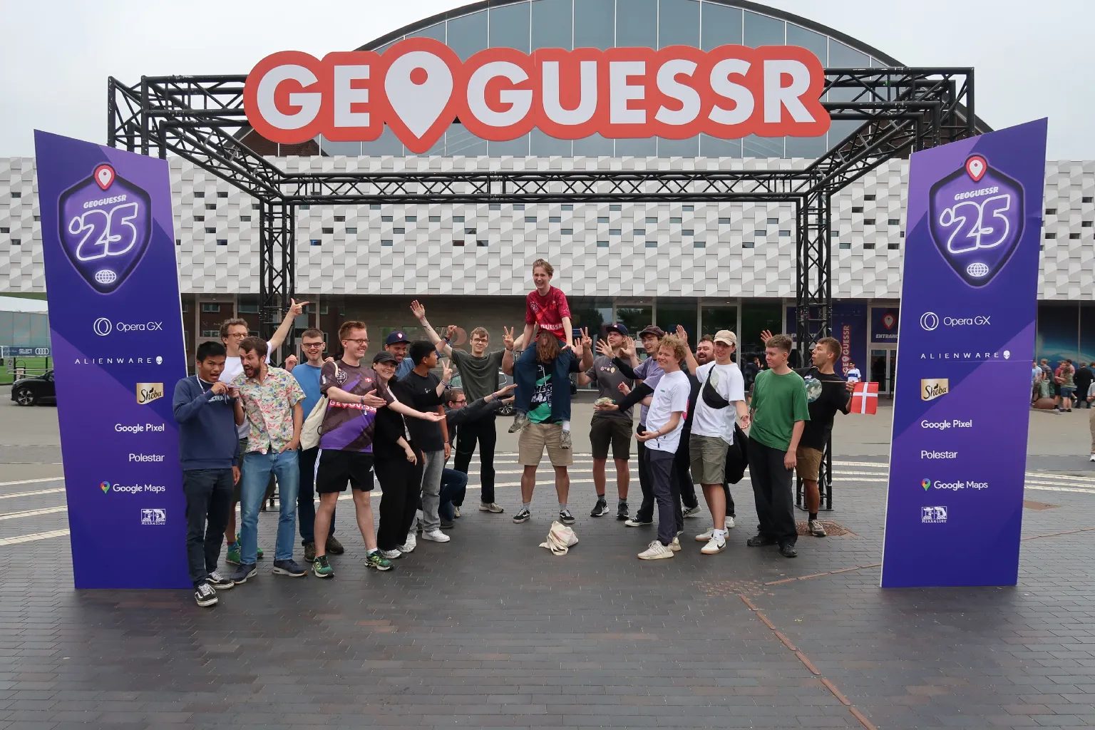 Danish GeoGuessr players cheering at the entrance to the GeoGuessr World Championship 2025 in Copenhagen. One of them sits on another’s shoulders.